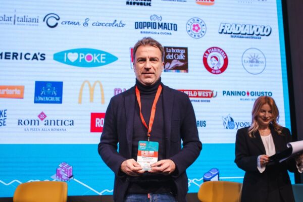 Food Service Powerlist: uomo con premio, marchi franchising food sullo sfondo.
