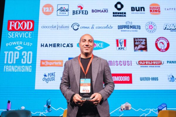 Top 30 Franchising: uomo con premio. Marchi food service sullo sfondo.