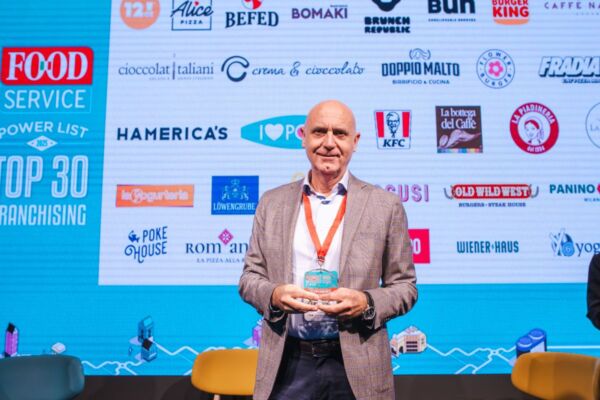 Top 30 Franchising: Uomo con premio, marchi food service sullo sfondo.