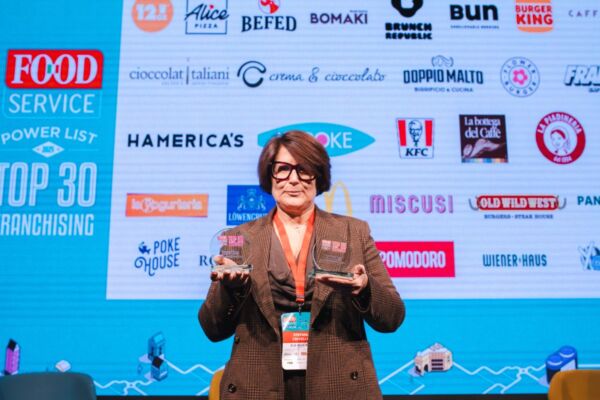 Premiazione top 30 franchising food service. Donna con premi, loghi ristorazione sullo sfondo.
