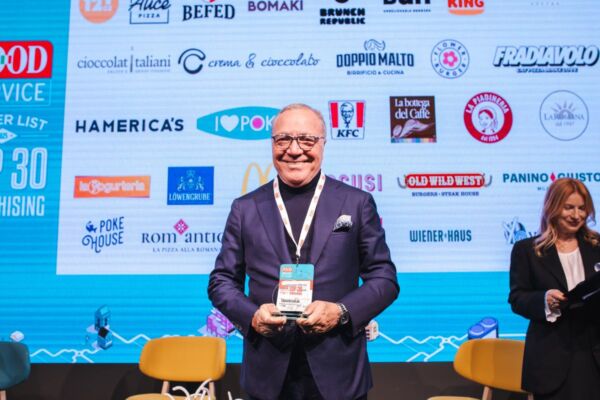 Premiazione Food Service Powerlist. Top 30 Franchising: uomo sorridente con premio, loghi ristorazione sullo sfondo.