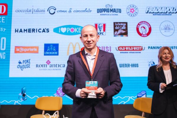 Premiazione Food Service Powerlist: uomo con premio franchising, marchi ristorazione sullo sfondo.