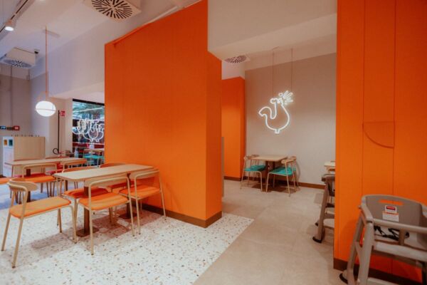 Interno del nuovo ristorante Popeyes a Roma. Tavoli, sedie colorate e logo pollo al neon.
