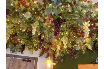 Allestimento indoor con vite: grappoli d'uva bianca e nera, foglie verdi e luci. Arte della vite per interni.