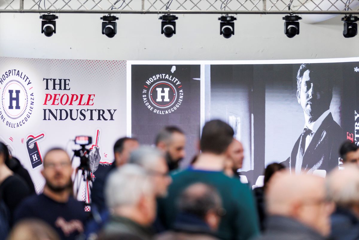 Presentazione Hospitality 2026. Stand fiera dell'accoglienza con pubblico. Logo Hospitality, persone, industria alberghiera.