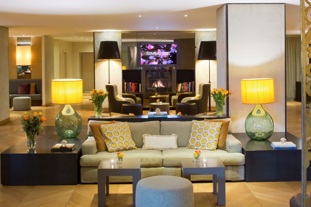 Lobby Starhotels: divano, lampade, caminetto. Design d'interni elegante. Fedegroup e Starhotels rafforzano la partnership.