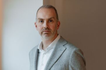 Ritratto di Kevin Derycke, uomo caucasico con giacca grigia e camicia bianca. Primo piano, sguardo diretto.