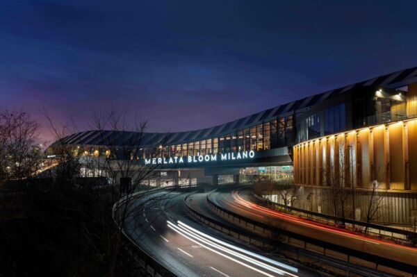 Esterno notturno del Merlata Bloom Milano. Vista del mall e traffico. Shopping a Milano.