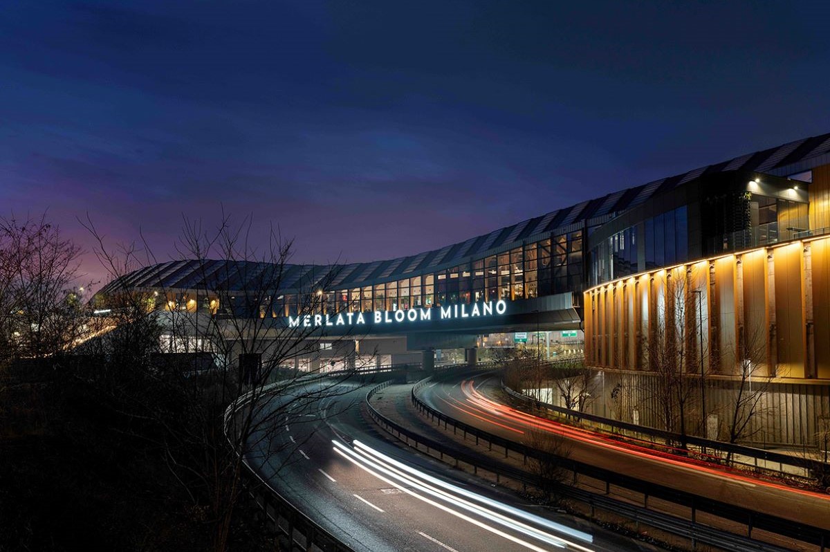 Esterno notturno del Merlata Bloom Milano. Vista del mall e traffico. Shopping a Milano.