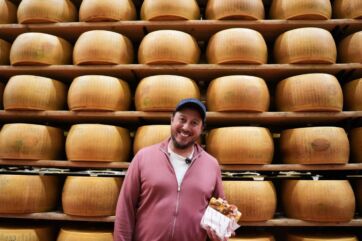 All'Antico Vinaio Parma: uomo sorridente con panino davanti a scaffali di Parmigiano Reggiano.