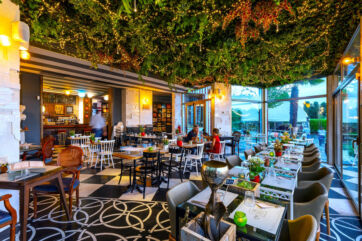 Ristorante Green Design: soffitto verde artificiale, luci, tavoli apparecchiati. Design d'interni elegante e accogliente.