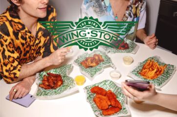 Wingstop debutta a Milano: amici gustano alette di pollo, patatine fritte e salse. Logo Wingstop in evidenza.