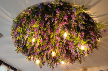 Design ristorante green: lampadario floreale con glicine viola e lampadine a bulbo. Illuminazione naturale.