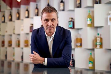 Marco Ferrari, CEO Disaronno Group. Ritratto aziendale con liquori sullo sfondo.