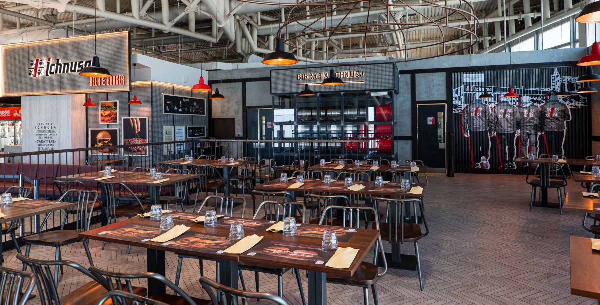 Interno di Ichnusa Beer & Burger, Chef Express all'Aeroporto di Cagliari. Tavoli apparecchiati e insegna Ichnusa.