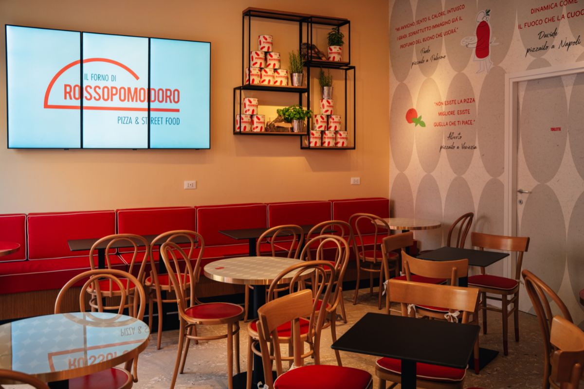Interni del Forno di Rossopomodoro: tavoli, sedie rosse e divanetti. Design accogliente per gustare pizza e street food.