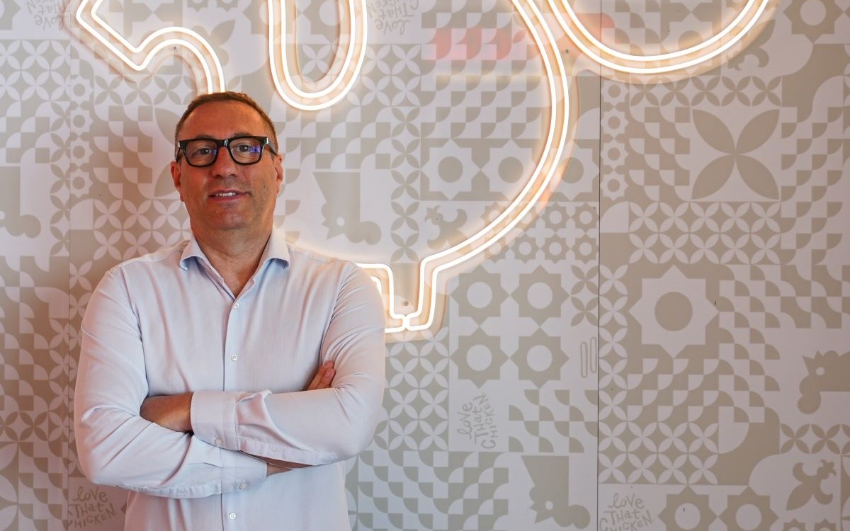 Alessandro Carluccio, General Manager di Popeyes Italia, davanti al logo luminoso in un ristorante Popeyes.