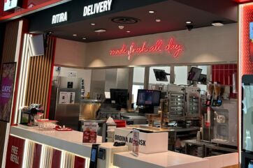 Interno del nuovo ristorante KFC a Castenaso, Emilia-Romagna, con area ritiro delivery e cucina moderna in vista.