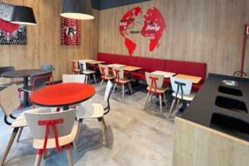 Interni del ristorante KFC a Reggio Calabria con tavoli, sedie moderne e decorazione murale a tema mondo.