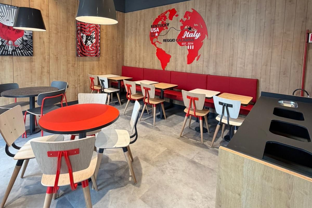 Interni del ristorante KFC a Reggio Calabria con tavoli, sedie moderne e decorazione murale a tema mondo.
