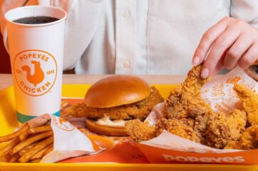 Menu Popeyes in Italia: panino con pollo fritto, patatine e bibita su vassoio giallo.