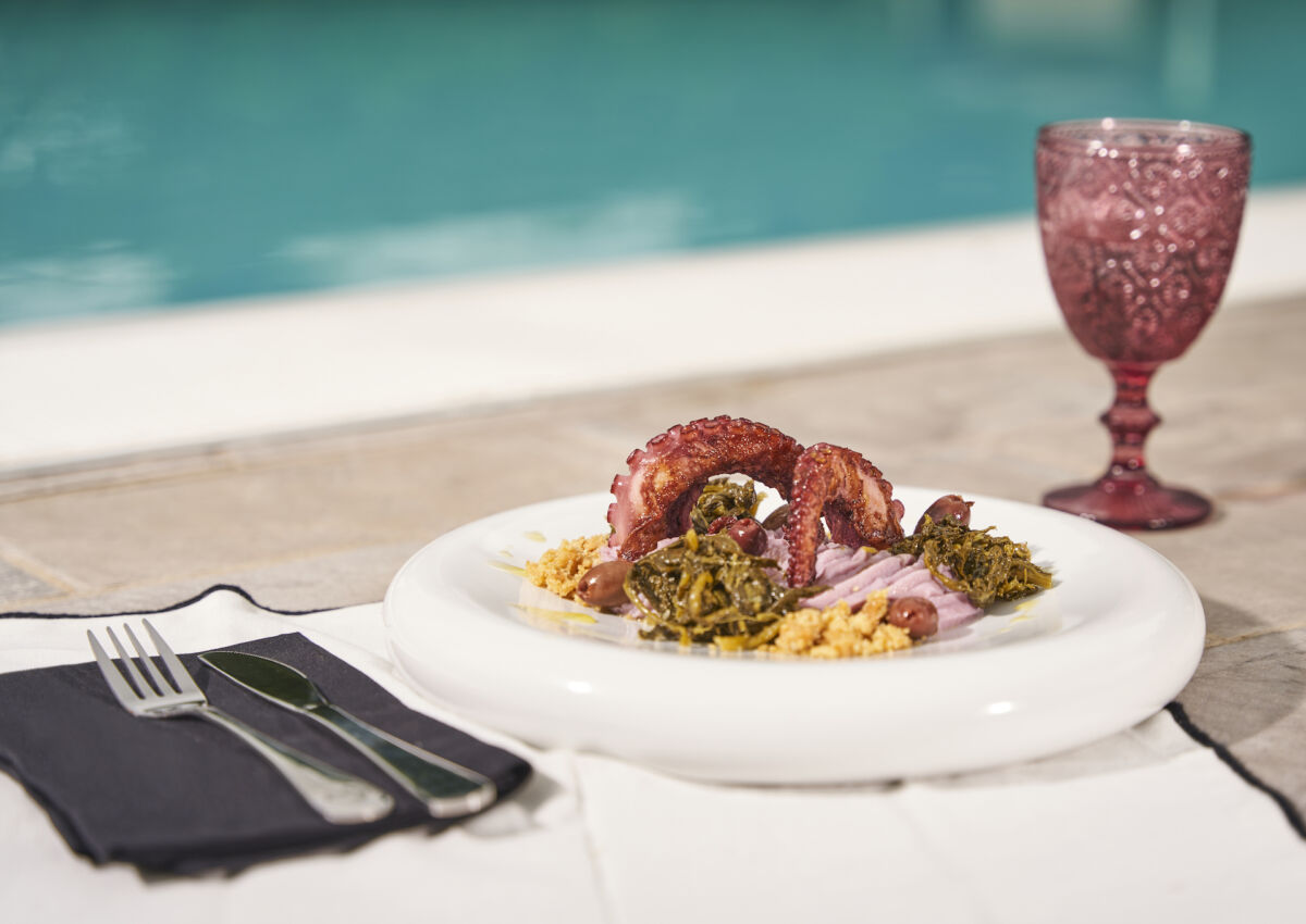 Piatto estivo con tentacoli di polpo BenServiti Menù, crema, olive e verdure, servito a bordo piscina con calice di vino.