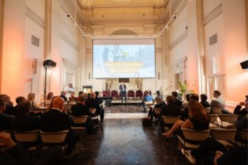 Conferenza AssoBirra sul mercato della birra: relatore sul palco davanti a una platea in una sala storica.