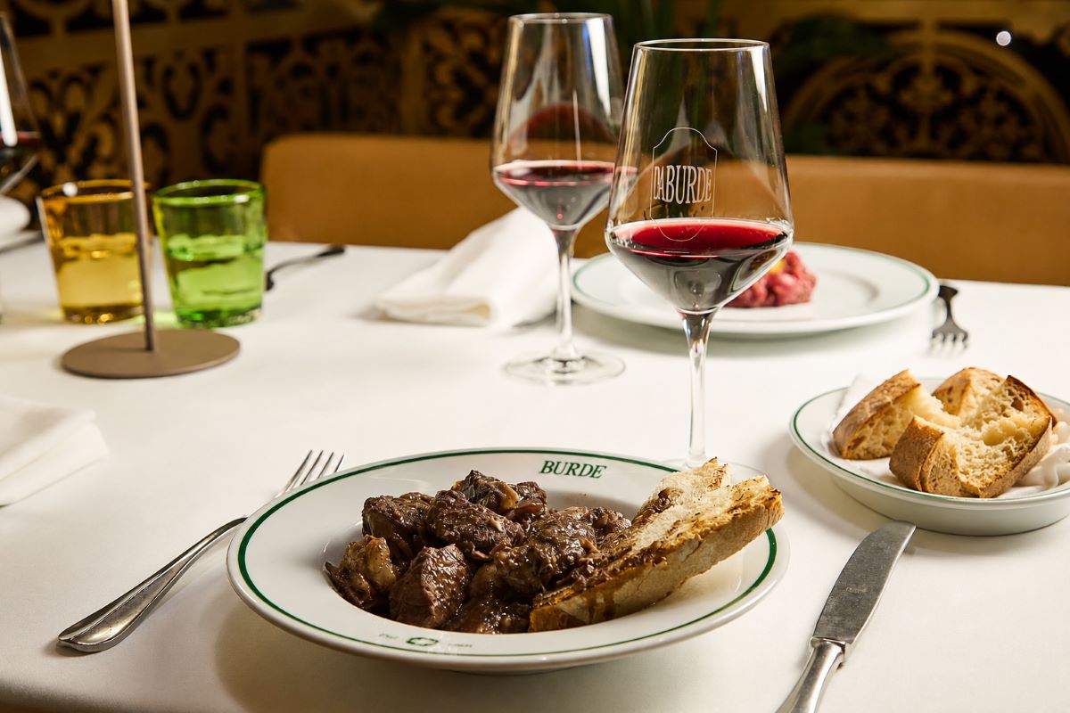 Piatti di carne tipica toscana e calici di vino rosso al ristorante Burde, serviti su una tavola elegante.