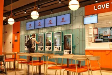Interno del ristorante Popeyes a Parma con totem digitali per ordinazioni, tavoli moderni e arredamento color arancio.