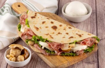 Piadina con Finocchiona, funghi e formaggio su tagliere di legno, ricetta regionale de La Piadineria.