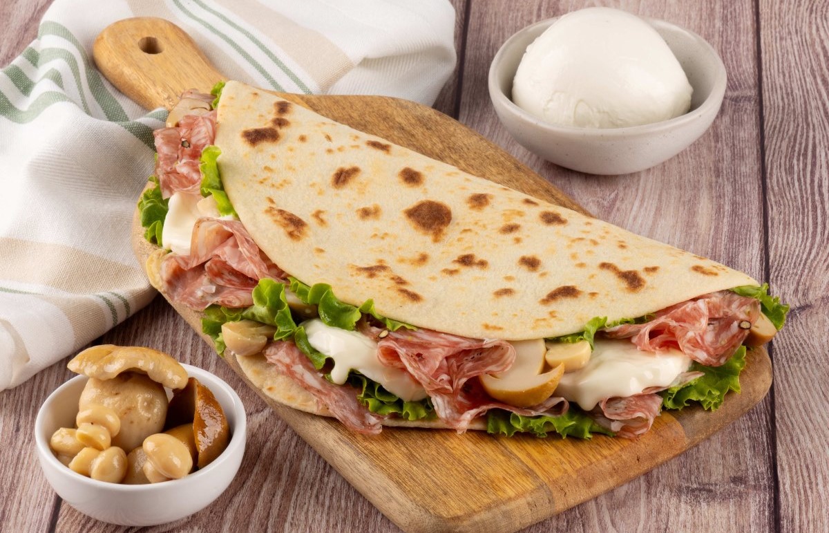 Piadina con Finocchiona, funghi e formaggio su tagliere di legno, ricetta regionale de La Piadineria.