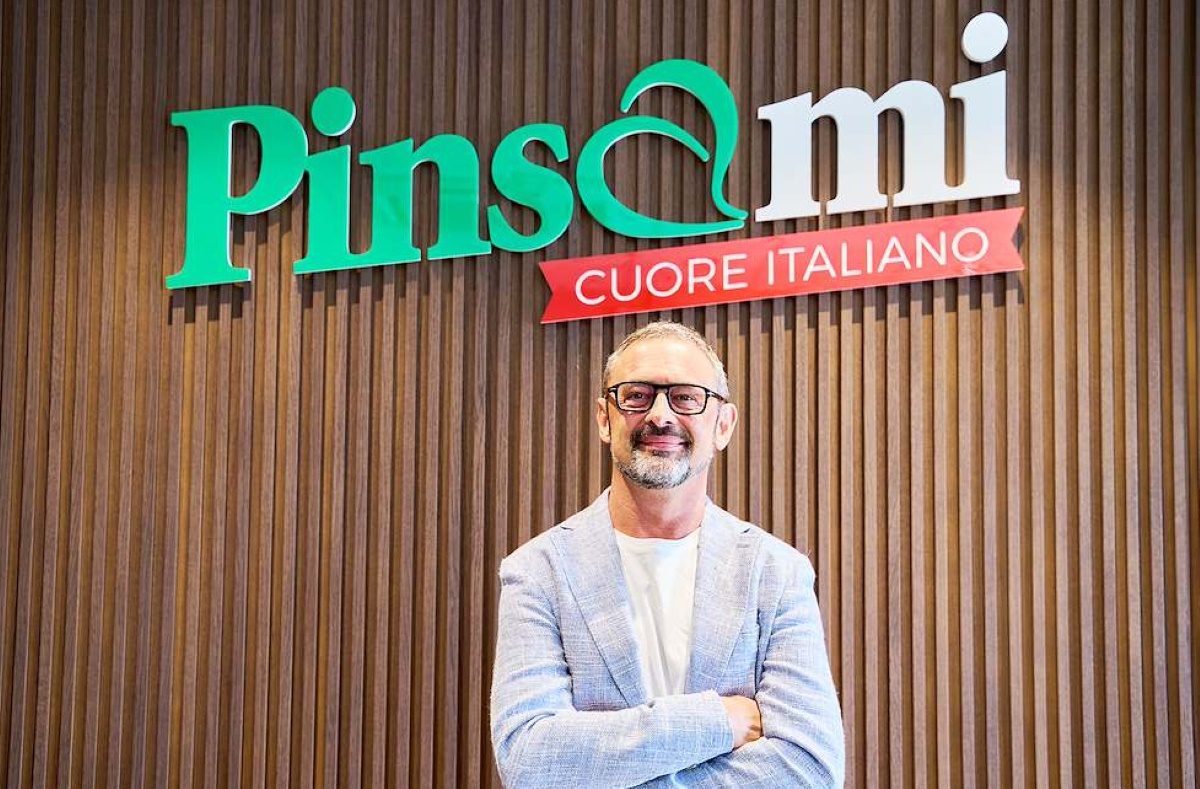 Mauro Dalle Vacche, fondatore di Pinsami, davanti al logo dell'azienda specializzata in pinsa romana di qualità.