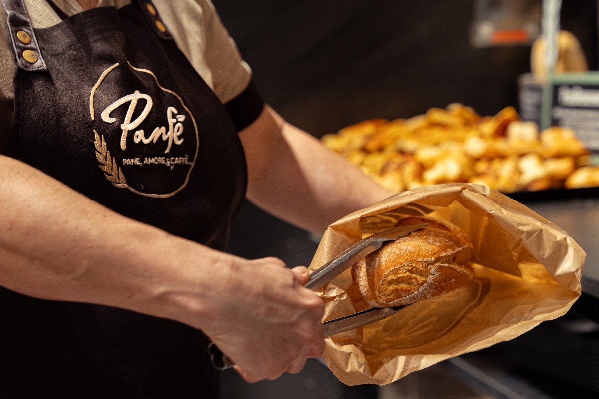 Addetto Panfé con grembiule nero imbusta pane artigianale fresco di qualità in un sacchetto di carta nel punto vendita.