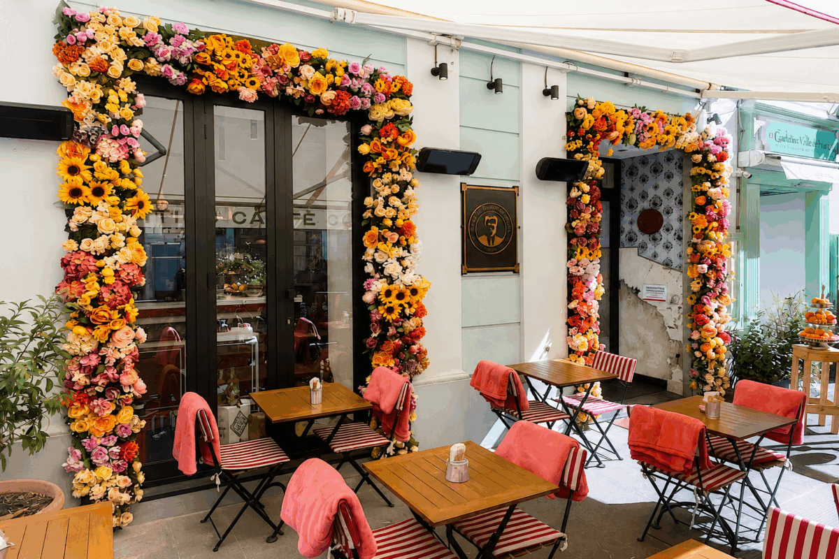 Green Restaurant Design: dehors di un locale decorato con archi di fiori colorati e tavolini in legno con sedie a righe.