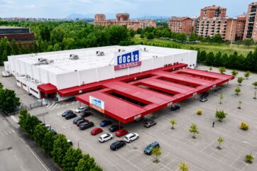 Veduta aerea del centro retail Docks Market con parcheggio e tettoie rosse, immobile oggetto di cessione immobiliare.
