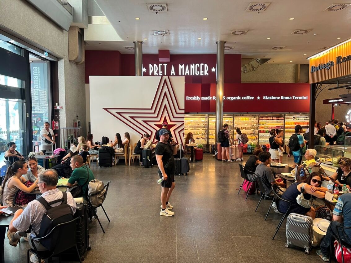 Nuovo punto vendita Pret A Manger all'interno della stazione Roma Termini con clienti ai tavoli e insegna luminosa.