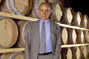 Vittorio Frescobaldi in giacca e cravatta davanti a una serie di botti di vino in una cantina storica.
