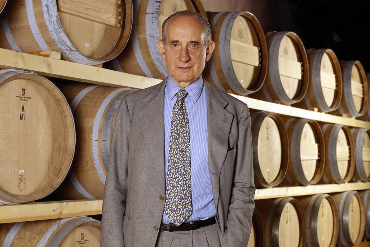 Vittorio Frescobaldi in giacca e cravatta davanti a una serie di botti di vino in una cantina storica.