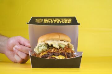 Panino del Futuro di Smash Tag servito in una scatola nera su sfondo giallo, burger gourmet con formaggio e verdure.