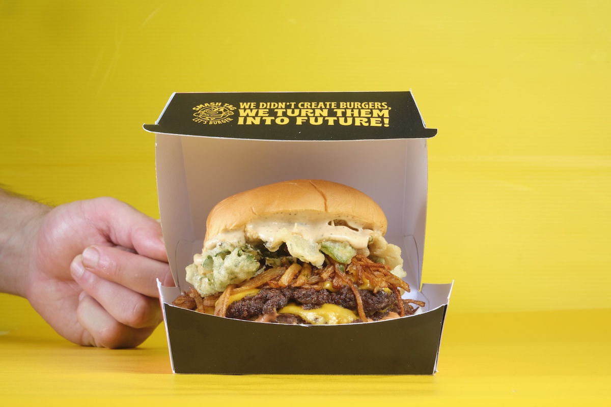 Panino del Futuro di Smash Tag servito in una scatola nera su sfondo giallo, burger gourmet con formaggio e verdure.