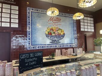 Interni di Antica Gelateria Matteo a Milano con piastrelle decorate, menu dei gusti e lavagna con sorbetto al cedro.