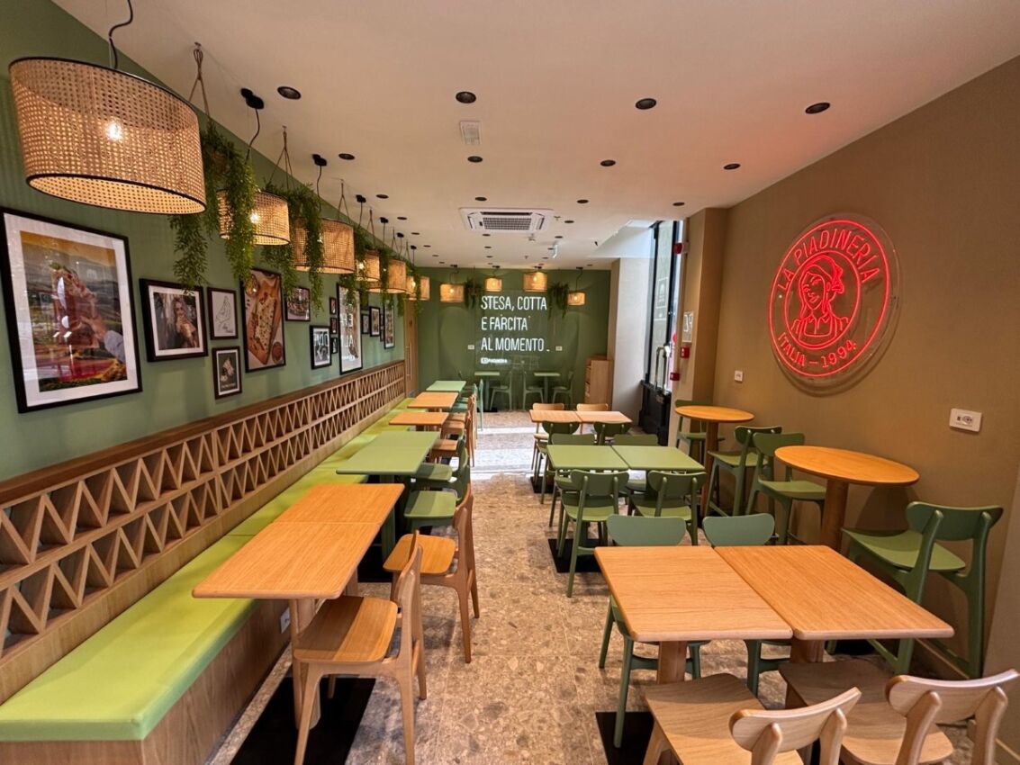 Interni del punto vendita La Piadineria alla Stazione Centrale di Milano con tavoli, sedie e insegna al neon rossa.