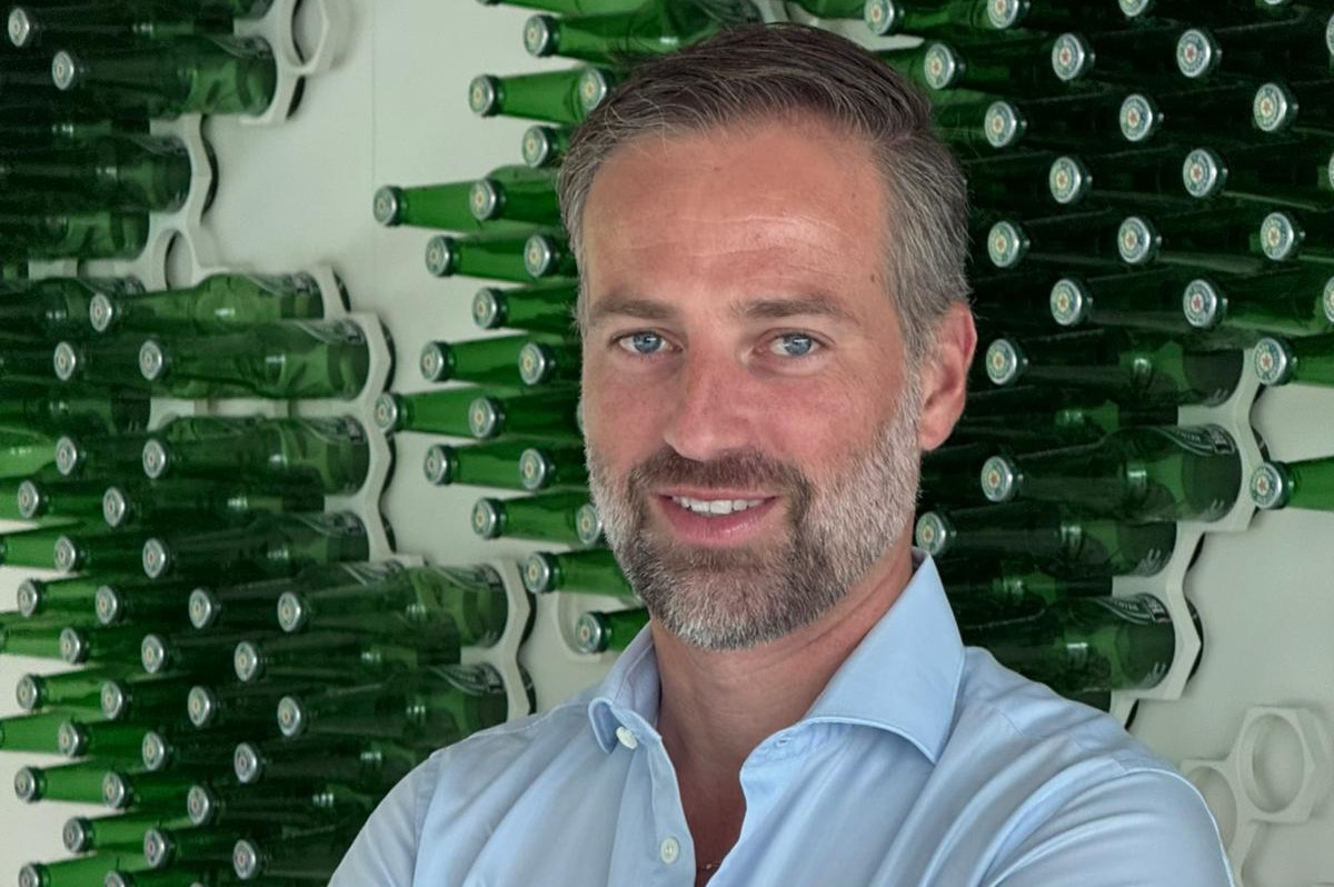 Paul Schalekamp, Amministratore Delegato di Partesa, davanti a una parete decorata con bottiglie di birra verdi.