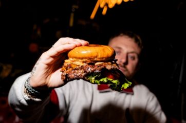 Uomo mostra un grande hamburger gourmet Duccio Smash Meat Sushi a Torino, pronto per il franchising