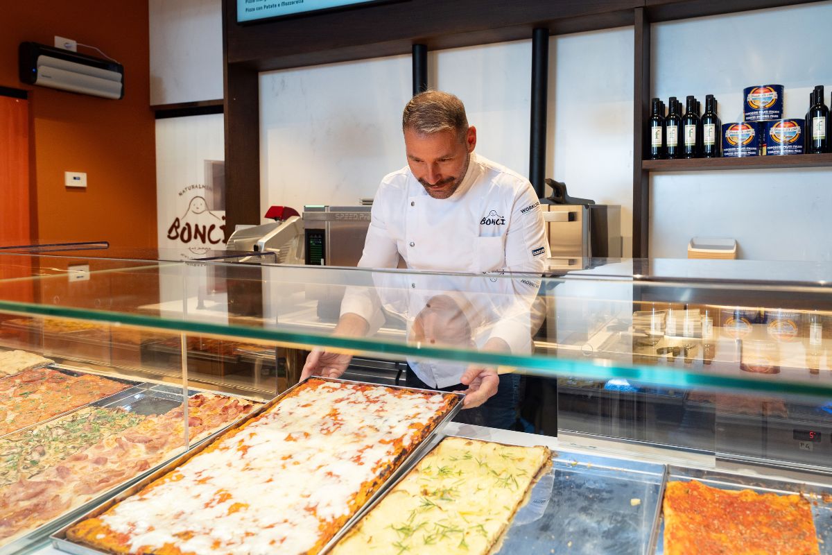 Gabriele Bonci in divisa bianca sistema la pizza al taglio nel banco espositivo del locale Bonci a Roma Termini.