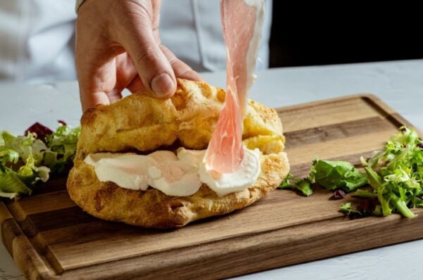 Panino con uovo e bacon del Gruppo Rispo, surgelati: mano aggiunge ingredienti su tagliere di legno