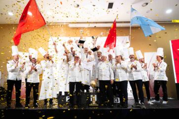 Podio chef: vincitori festeggiano con bandiere e coriandoli. Competizione culinaria, successo, team di cucina.