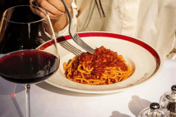 Cucina italiana: piatto di pasta al ragù e bicchiere di vino rosso. Patrimonio UNESCO.
