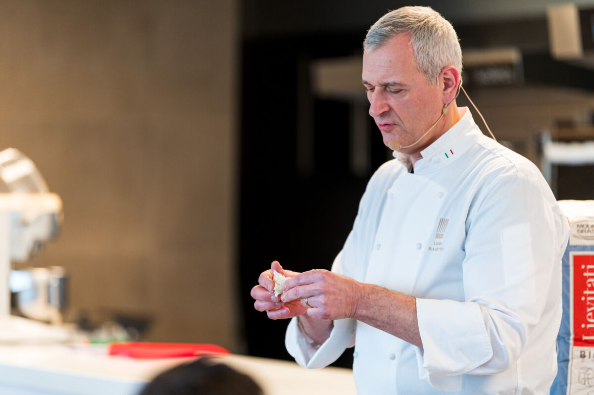 Chef italiano in divisa bianca lavora pasta. Esperto di panificazione e lievitati. Cucina italiana di alta qualità.