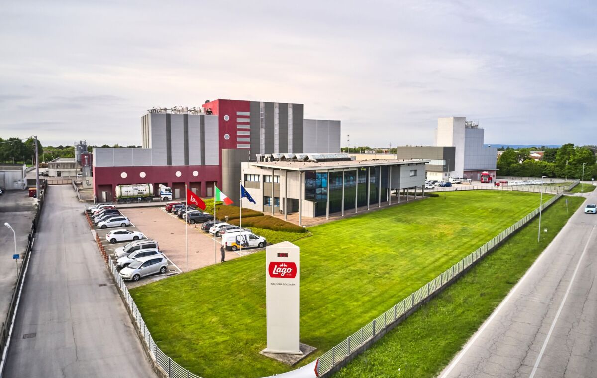 Stabilimento Lago dal 1968. Industria dolciaria italiana, sede aziendale con parcheggio e bandiere.